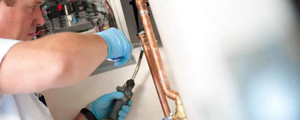 Water heater repair technician testing copper pipe connections and controls in Miami, FL